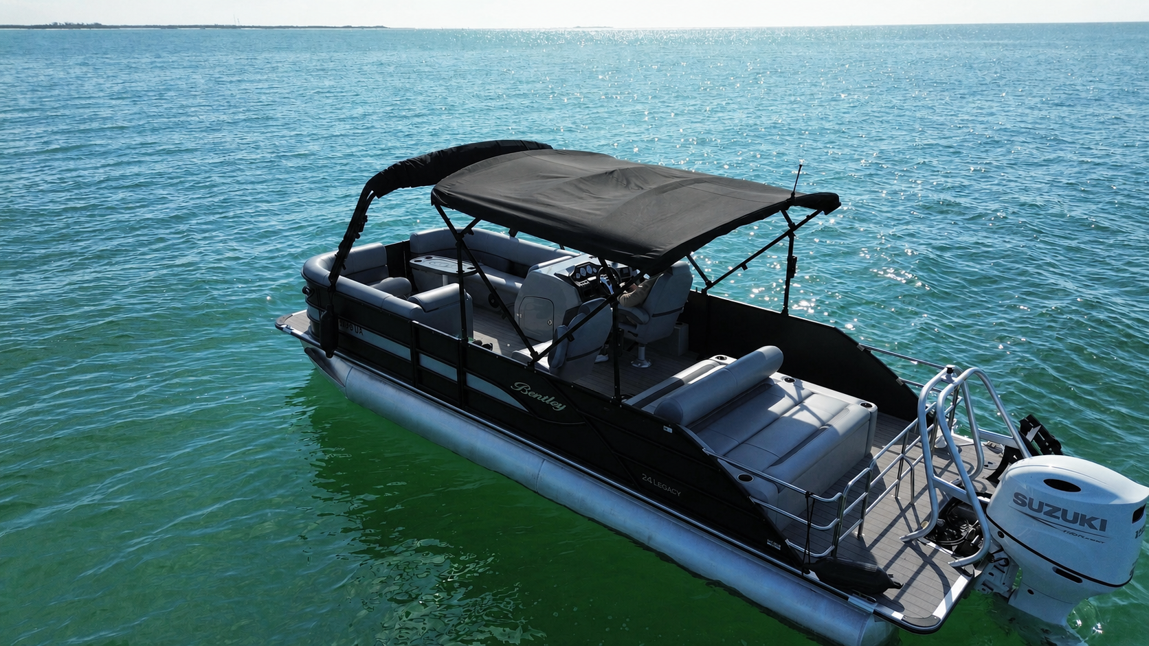 Aerial close view of the Bentley tritoon’s empty seating, dual bimini tops, helm, and Suzuki motor