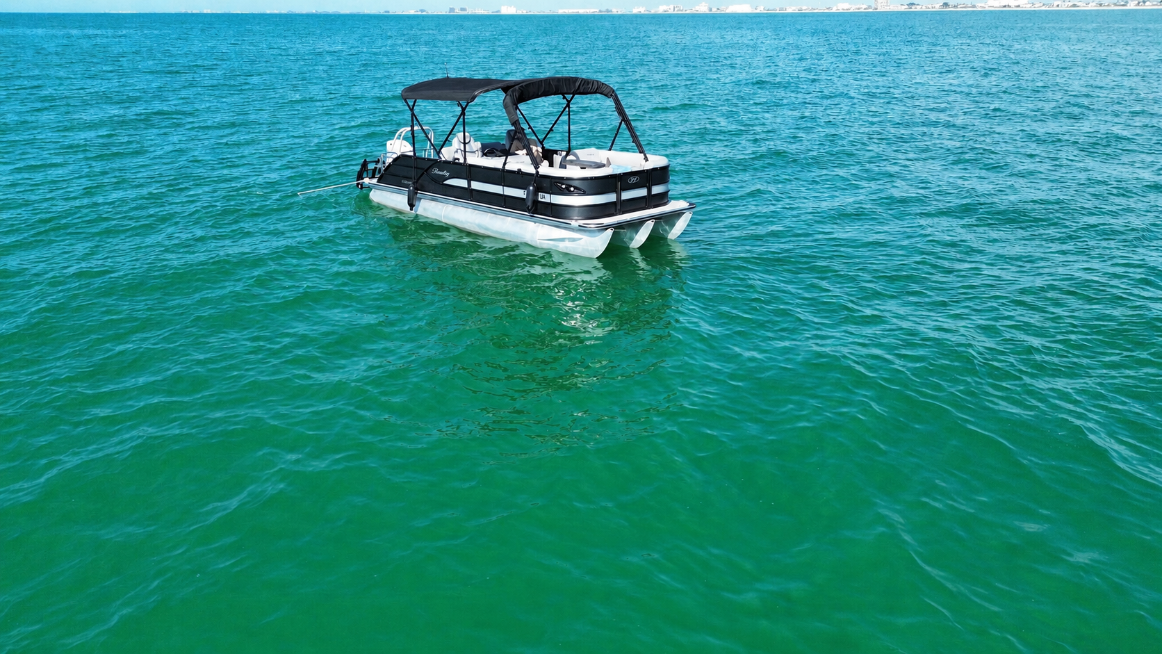 Black Bentley tritoon floating in turquoise Gulf water, photographed from the air